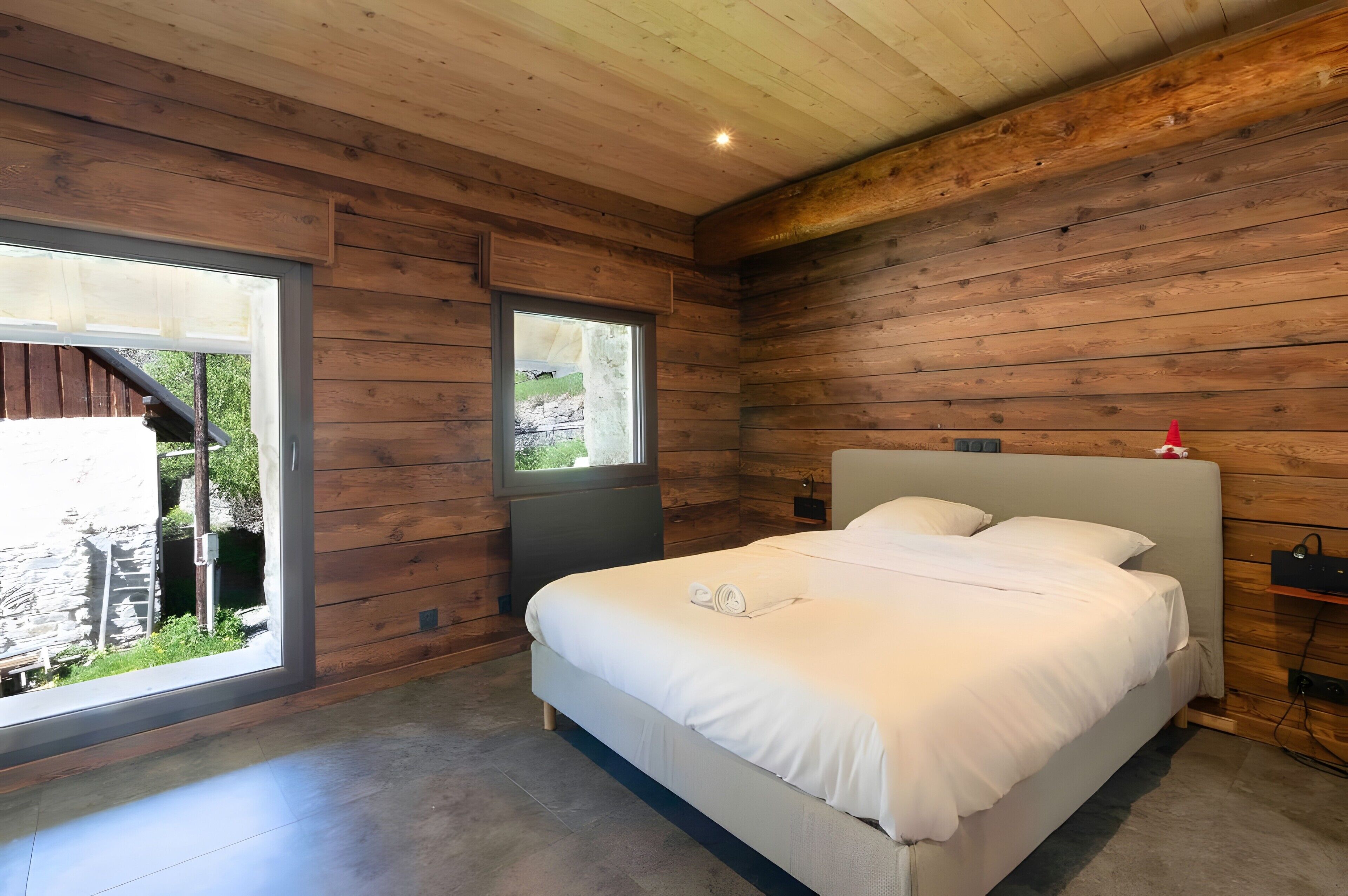 Quarto com uma cama grande, uma janela e paredes de madeira.