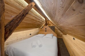 A narrow, wooden-paneled room with a single bed, pillows, and rolled towels.