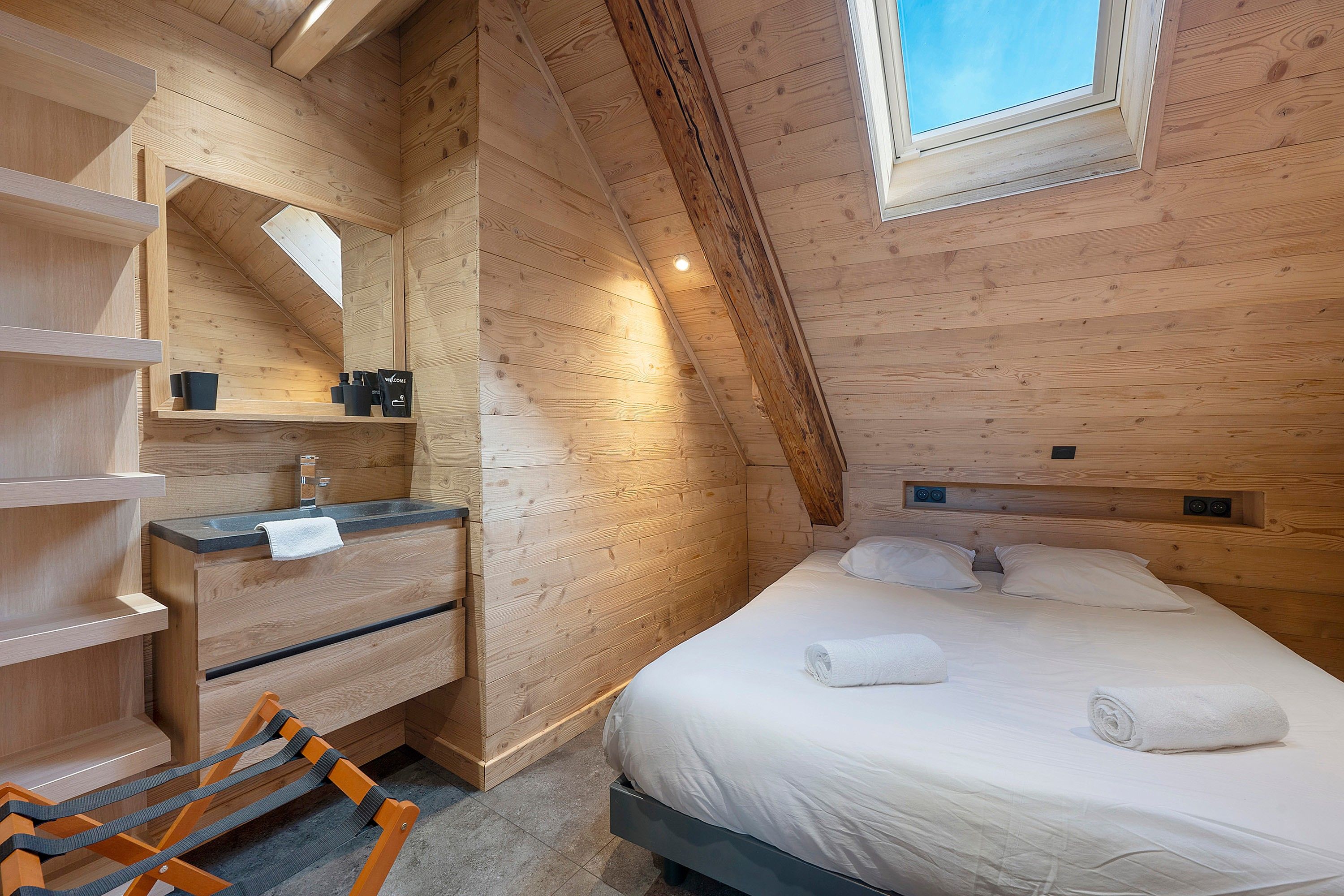 Ein Zimmer einer Holzhütte mit einem Bett, einem fest eingebauten Schreibtisch, einem Spiegel und einem Fenster.