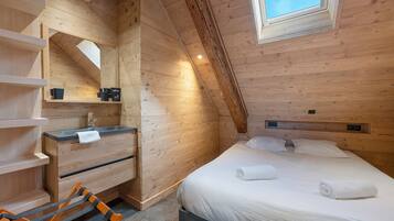 A wooden cabin room with a bed, a built-in desk, a mirror, and a window.