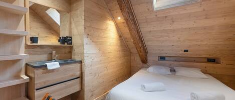 Ein Zimmer einer Holzhütte mit einem Bett, einem fest eingebauten Schreibtisch, einem Spiegel und einem Fenster.