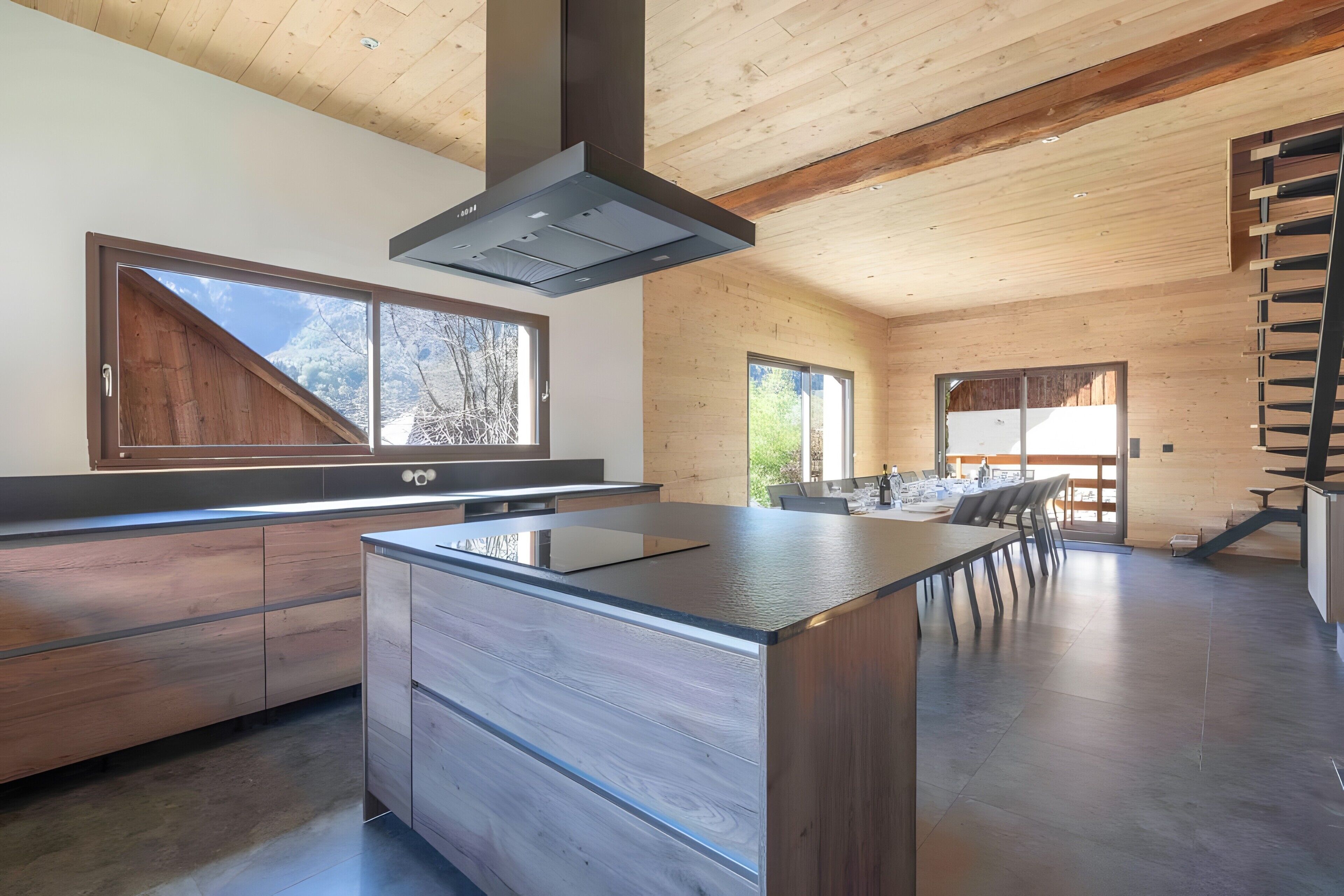 A modern kitchen with a central island, wooden cabinetry, and a large window overlooking a snowy landscape.