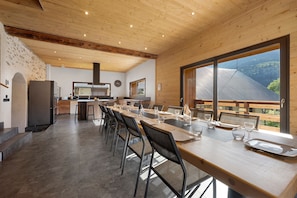 A modern kitchen with a large island, wooden ceiling, and a view of a forest through a large window.