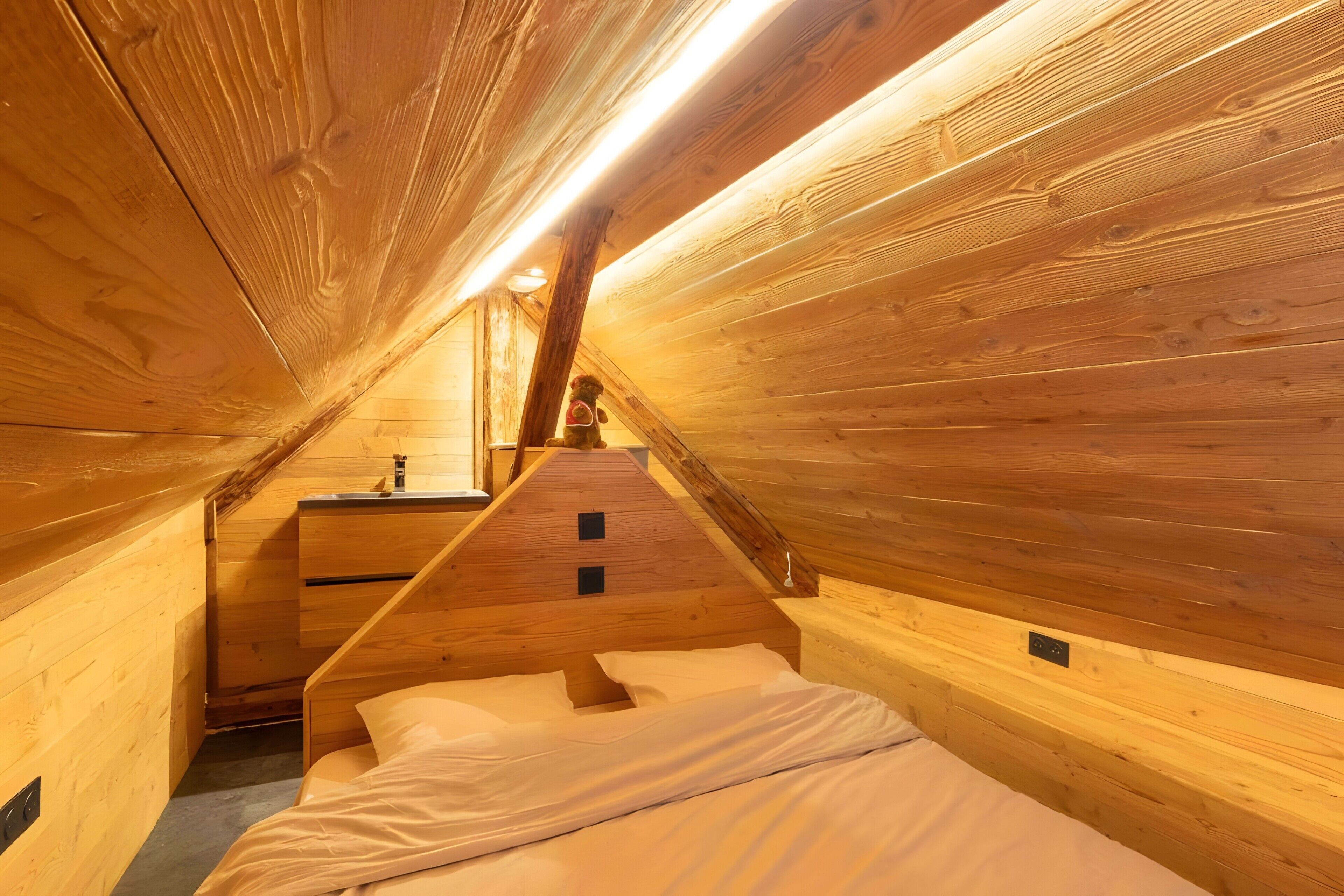 Un intérieur en bois avec un plafond en pente, un lit, une petite table et une chaise.
