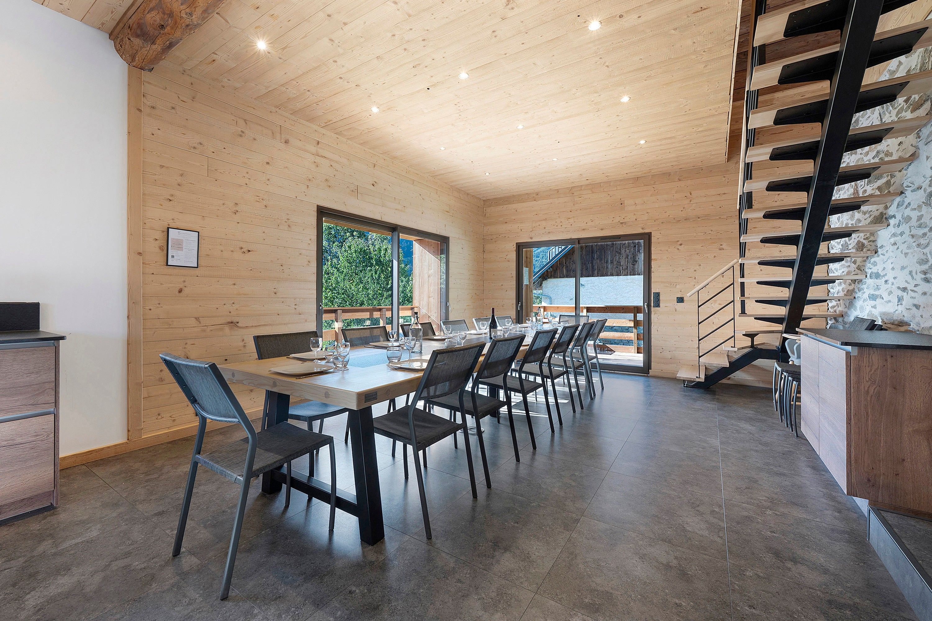 Un interior moderno con techo de madera, un comedor con sillas y mesa, y una escalera con barandilla de metal.