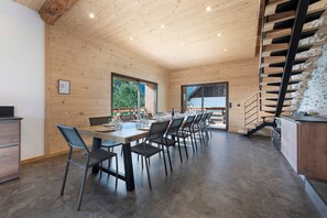 Un interior moderno con techo de madera, un comedor con sillas y mesa, y una escalera con barandilla de metal.
