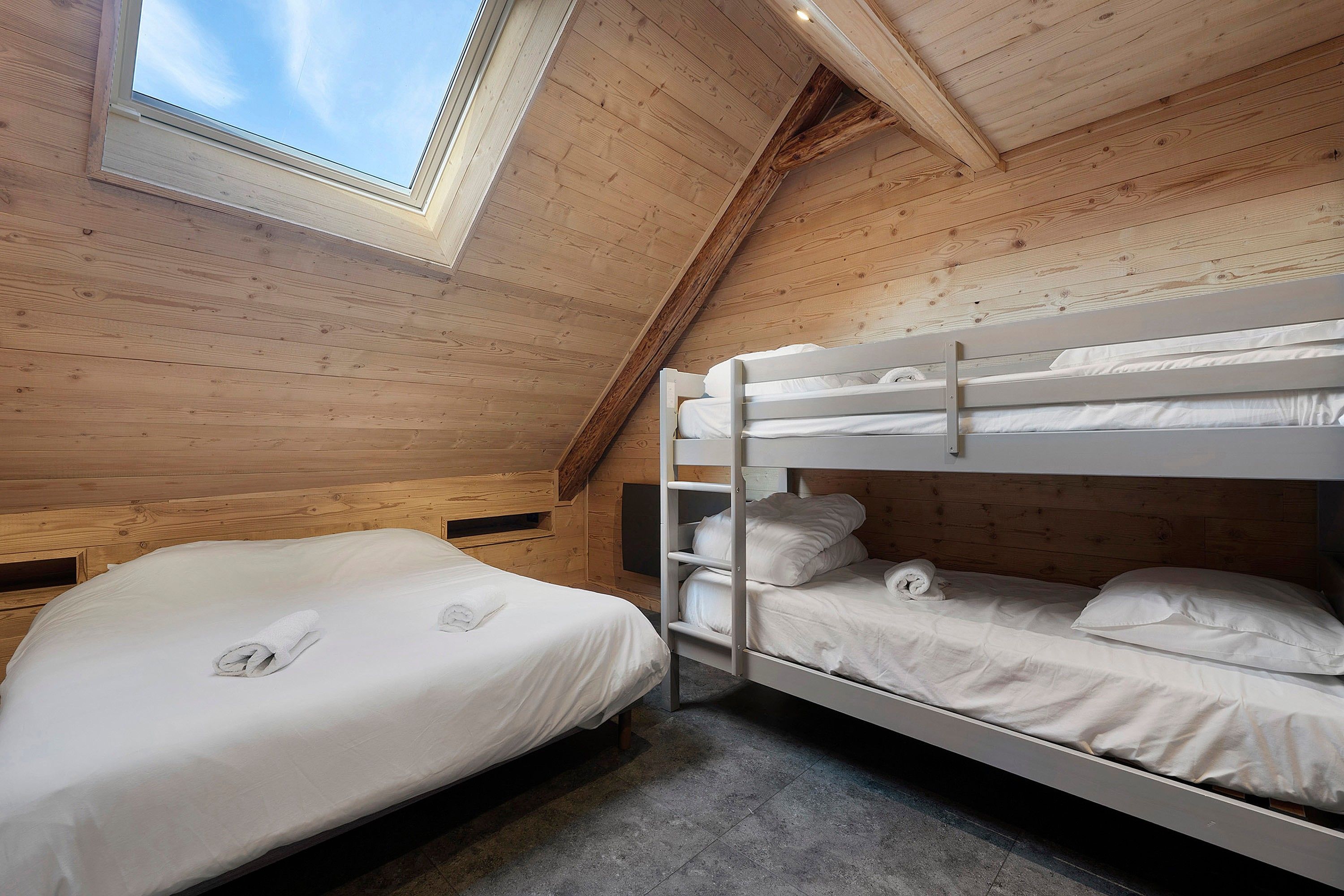 A bunk bed room with a skylight, wooden walls, and a concrete floor.