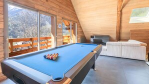 Una mesa de billar en una sala de madera con ventanas grandes y vistas a árboles.