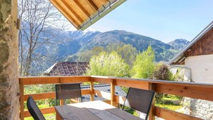 Una terraza de madera con una mesa y sillas, con vistas a un paisaje montañoso.