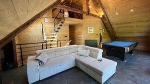 Un espacio tipo loft con sofá seccional, mesa de billar y escalera que lleva a un nivel superior.