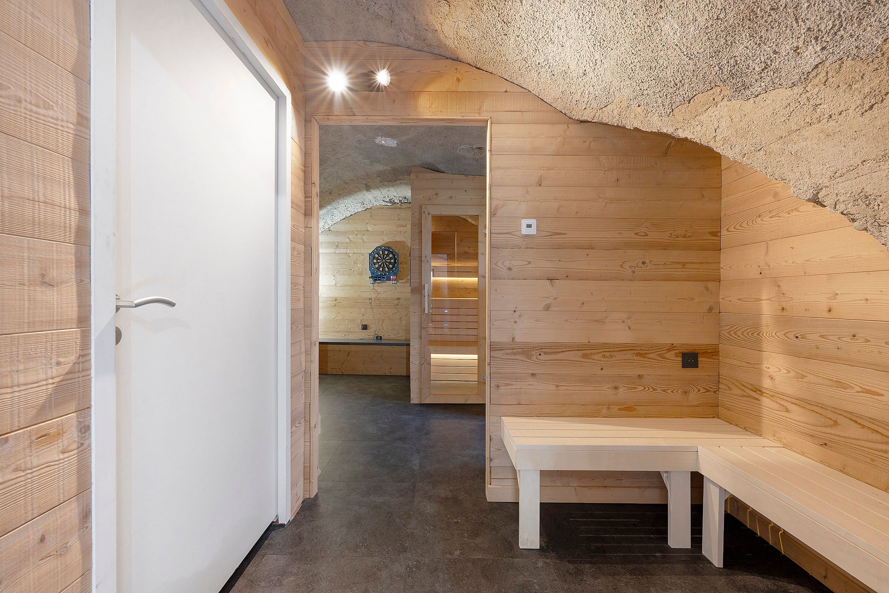 Un sauna avec des murs et des bancs en bois, une porte et un plafond doté d’un éclairage encastré.