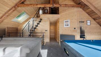 Ein gemütliches Dachzimmer mit Billardtisch, Sofa und einer Wendeltreppe zu einer Erkerzone.