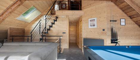 A cozy attic room with a pool table, a sofa, and a staircase leading to a loft area.
