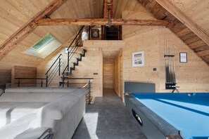 A cozy attic room with a pool table, a sofa, and a staircase leading to a loft area.