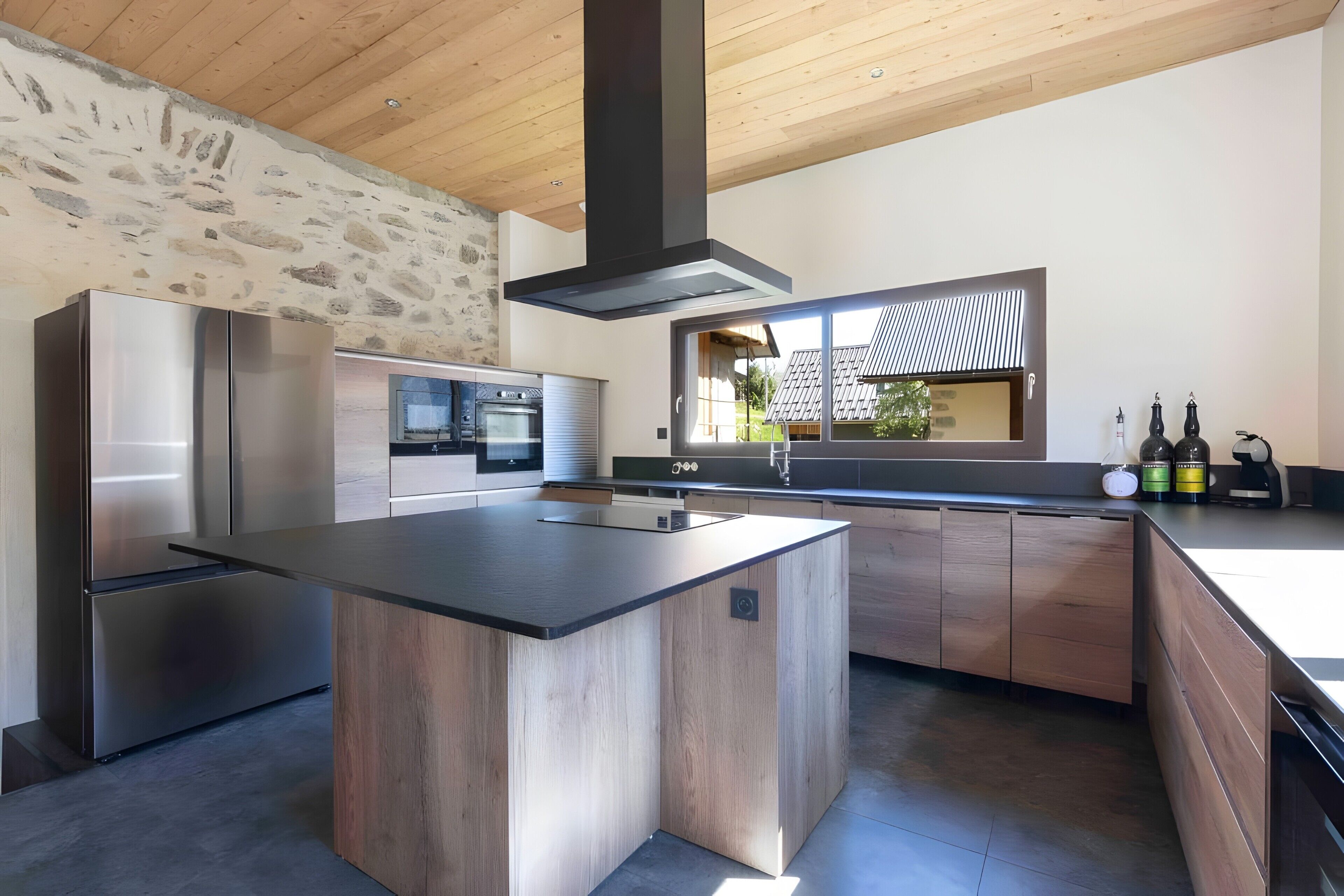 Uma cozinha moderna com ilha central, eletrodomésticos de aço inoxidável e parede com detalhe em pedra.