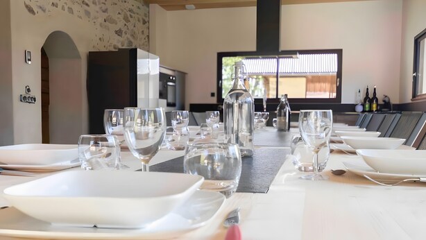 Un comedor con varias mesas dispuestas para una comida, un ventanal con persianas y una pared de piedra.