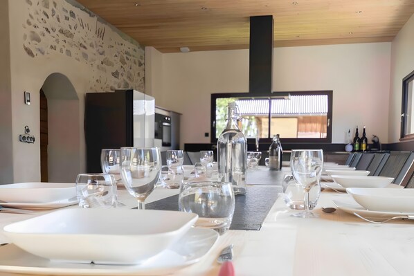 A dining area with multiple tables set for a meal, a large window with blinds, and a stone wall.