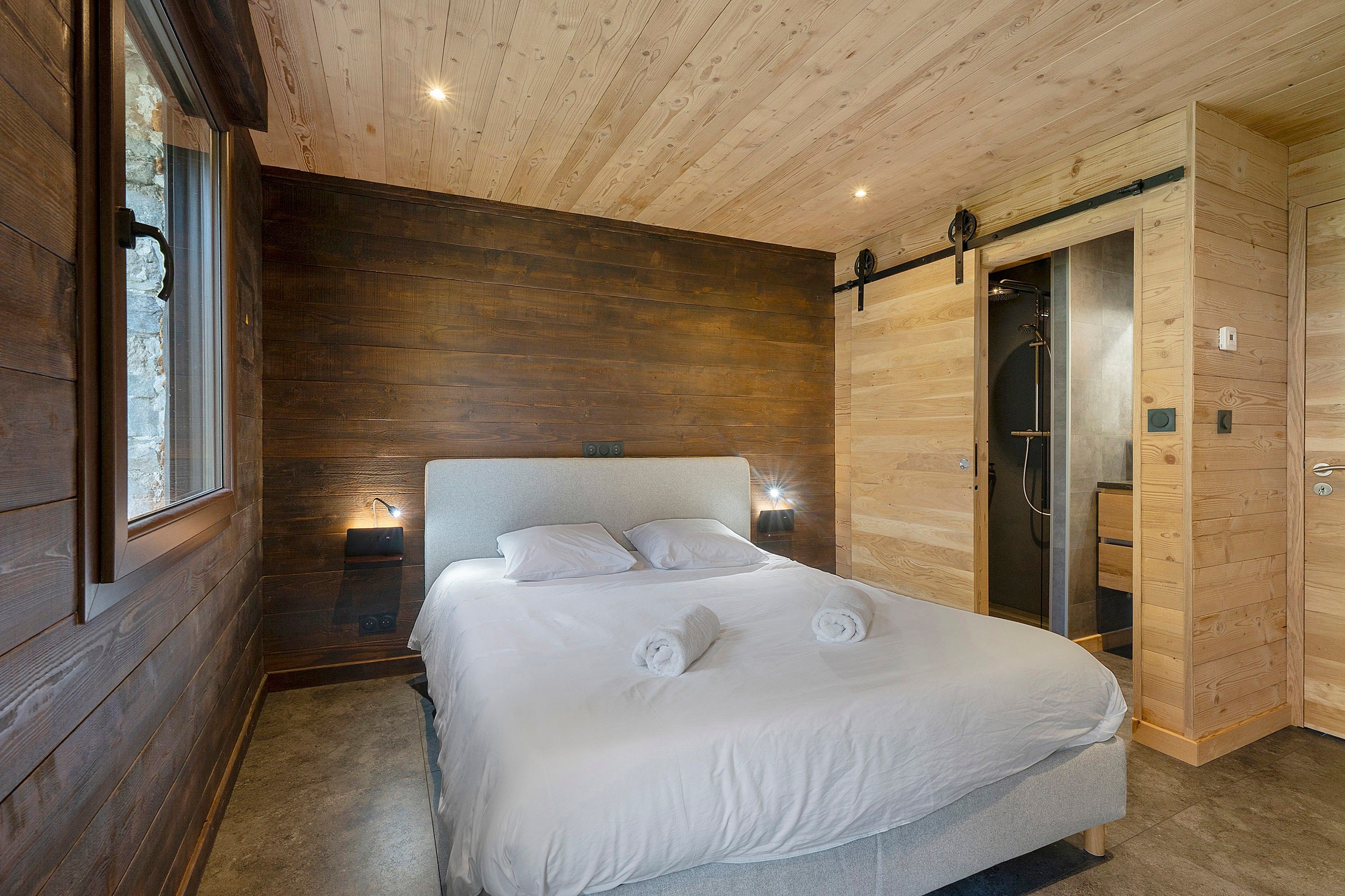 A bedroom with a large bed, wooden walls, a sliding door, and a window.