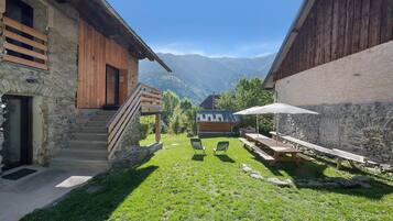 A rustic outdoor area with a wooden staircase leading to a wooden door, a picnic table with chairs, and a stone wall.