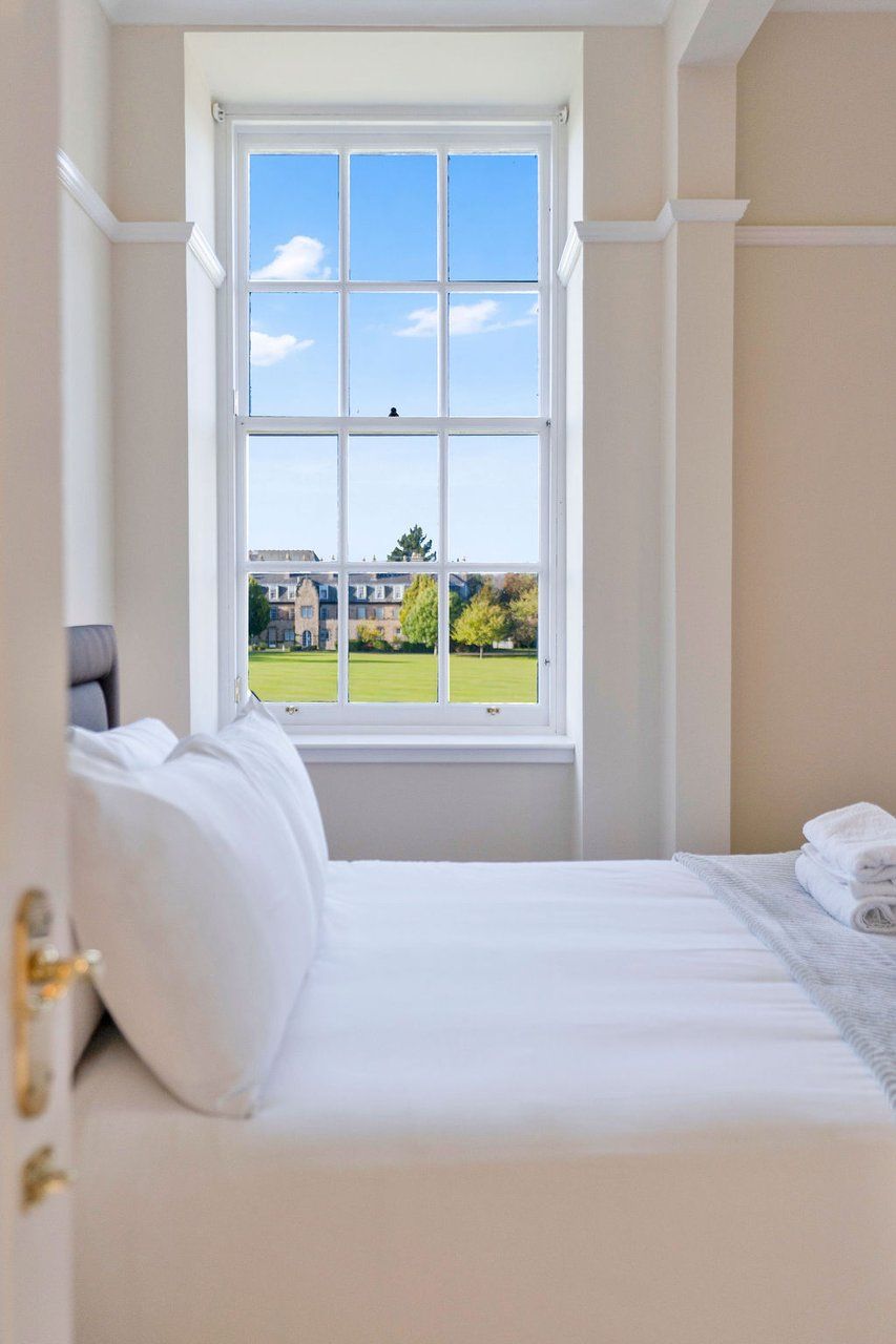 Un dormitorio con un ventanal grande, una cama y vistas a un edificio y árboles.