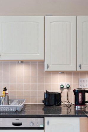 A kitchen with white cabinets, a Bosch dishwasher, a black toaster, and a kettle on the counter. - GuestReady - Spacious 1bed in Newington, Edinburgh (Edinburgh)