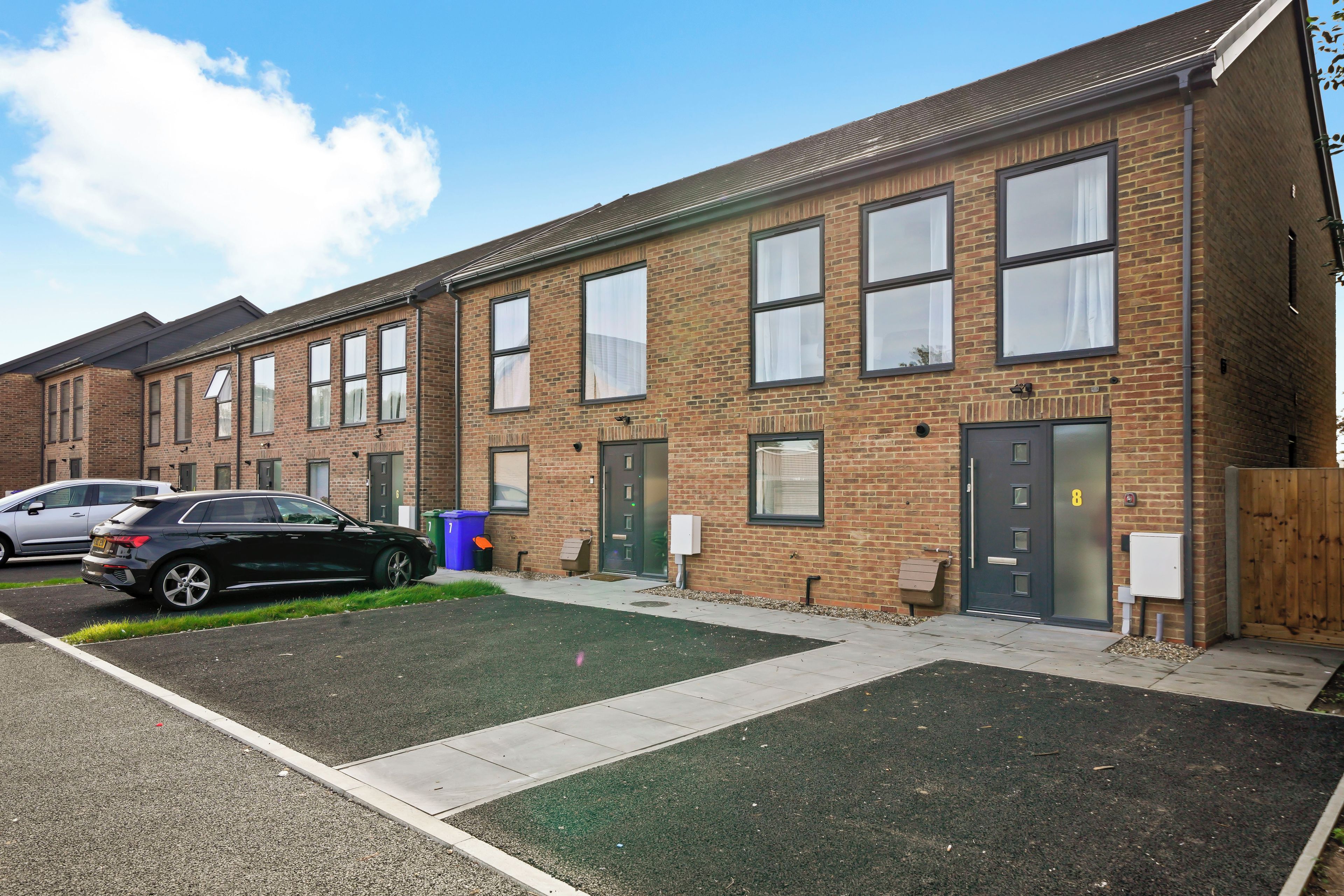 A row of brick townhouses with a parking area in front.