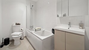 Moderni kylpyhuone, jossa on kylpyamme, wc ja suuri peili pesualtaan yläpuolella.