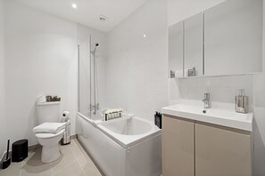 Ein modernes Badezimmer mit einer Badewanne, Toilette und einem großen Spiegel über dem Waschbecken.