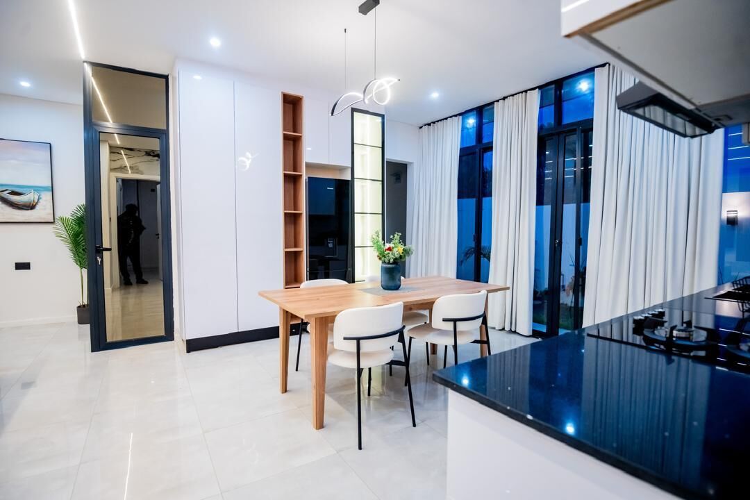 Una cocina moderna con una isla central, un comedor con mesa y sillas de madera, y un ventanal con cortinas.