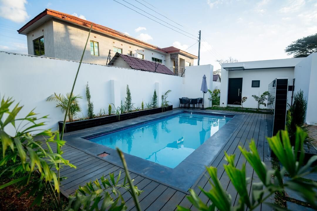 A swimming pool with a wooden deck, surrounded by a white wall and potted plants.