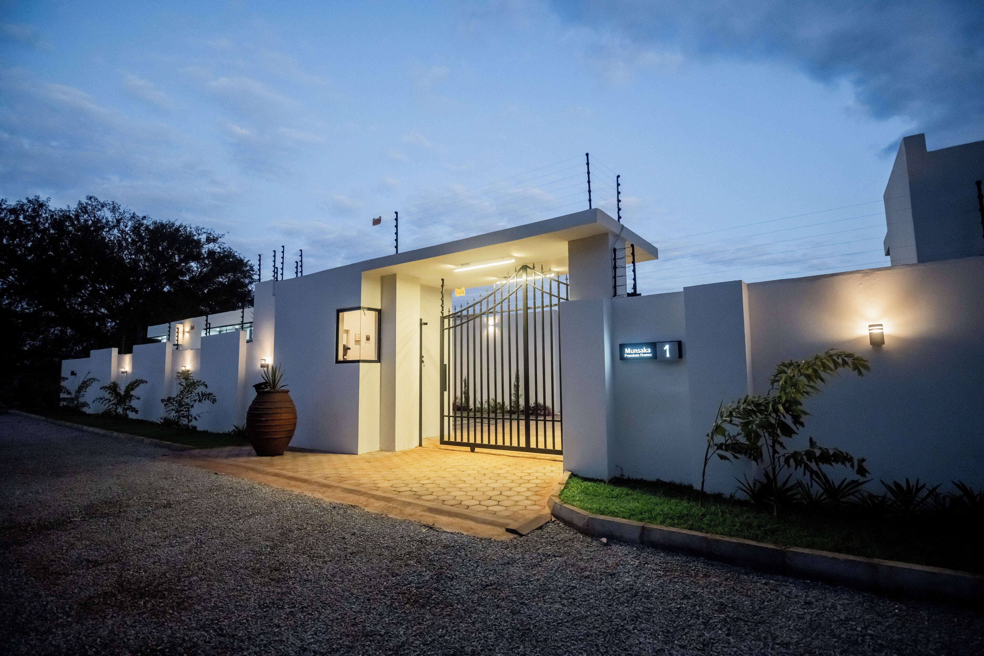A gated entrance to a modern building with a paved driveway and a large planter.