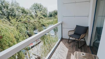 Uma varanda com vista para um rio e vegetação, uma cadeira de vime e piso de madeira.