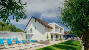 Una casa moderna de dos pisos con zona de piscina, mobiliario exterior y techo de paja.