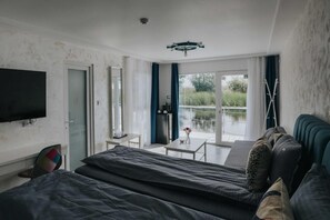 A hotel room with a bed, a TV, a balcony with a view of greenery, and a ceiling fan.