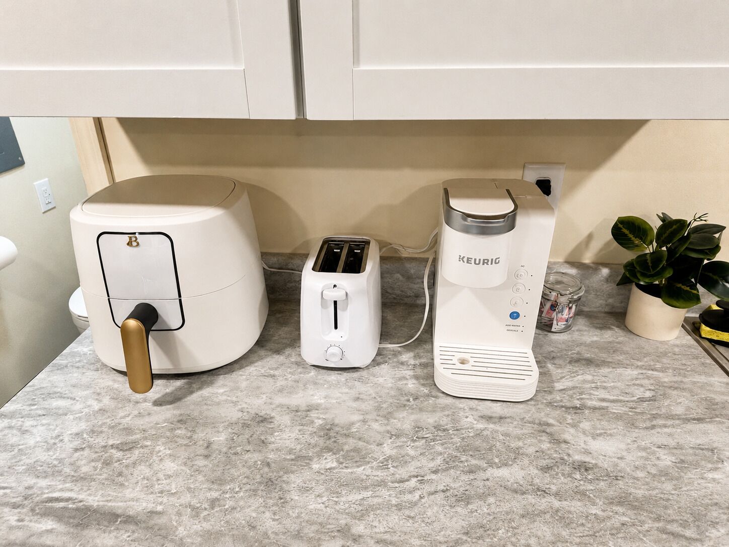 A kitchen with a coffee maker, toaster, and a kettle on a marble countertop.