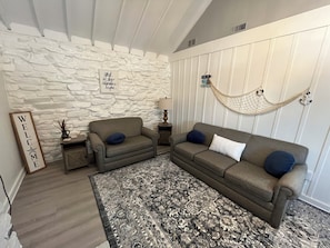 A living room with a stone wall, two sofas, a patterned rug, and a hammock.