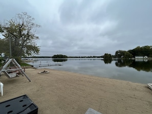 A lakeside view with a sandy beach, a swing set, and a dock extending into the water.