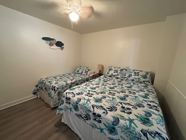 A room with two beds, a ceiling fan, and a wall-mounted light fixture.