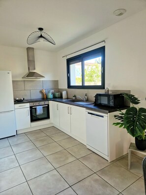 A modern kitchen with white cabinets, a built-in oven, a microwave, and a window above the sink. - The Catalan Cocoon – 3 bedrooms, garden & barbecue – sleeps 6 (Perpignan)