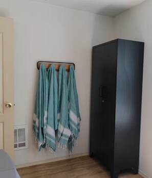 A room with a wardrobe, a coat rack with multiple items, and a vent on the wall.
