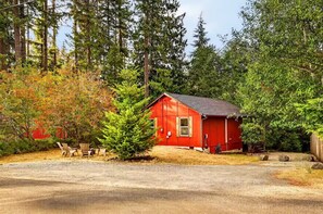 Eine kleine rote Holzhütte mit einer unbefestigten Auffahrt, umgeben von dichtem Wald.