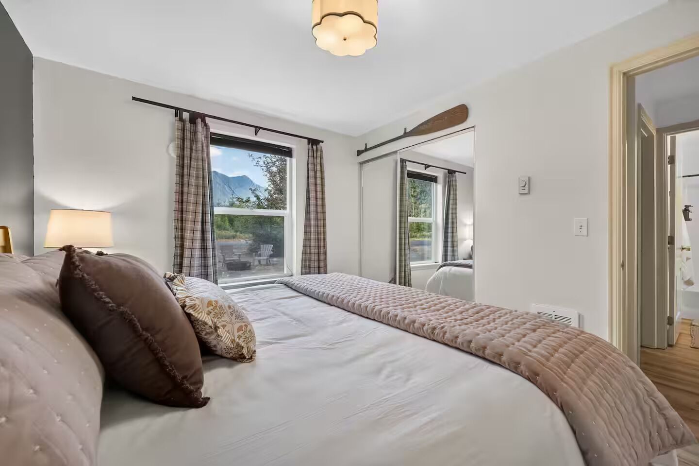 Un dormitorio con una cama grande, una ventana con cortinas, vistas al exterior y una lámpara en el techo.
