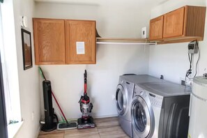 A laundry room with a washing machine, a vacuum cleaner, and wooden cabinets.