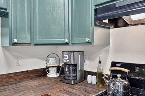 A kitchen with teal cabinets, a coffee maker, a kettle, salt and pepper shakers, and a bottle of oil on the counter.
