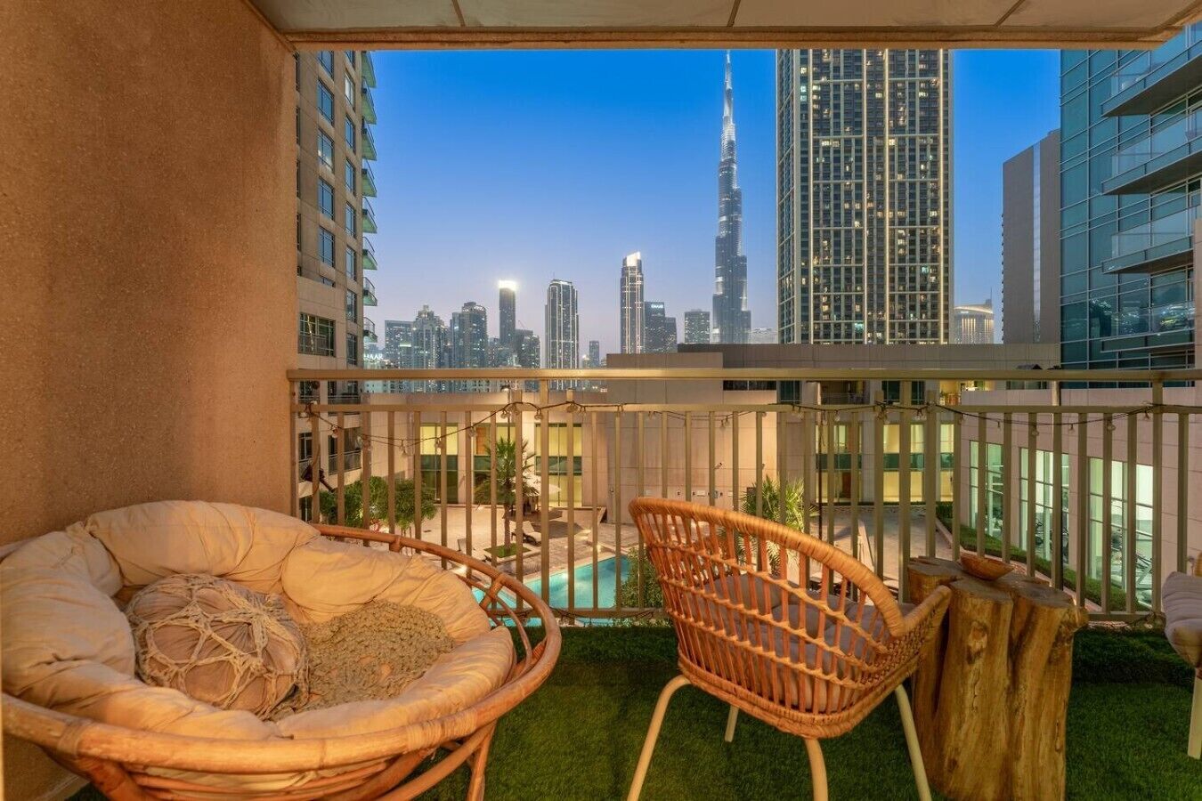 Ein Balkon mit Blick auf eine Stadtlandschaft, darunter ein markanter Turm, ausgestattet mit Korbstühlen und einem kleinen Pool.