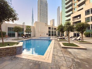 Ein Swimmingpool mit Liegestühlen und Blick auf ein hohes Gebäude im Hintergrund.