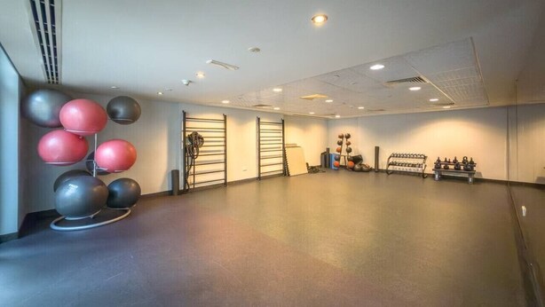 Ein geräumiges Zimmer mit ebenerdiger Ausstattung, Deckenleuchten und Trainingsgeräten, darunter ein Hantelständer und eine Sammlung Medizinbälle.