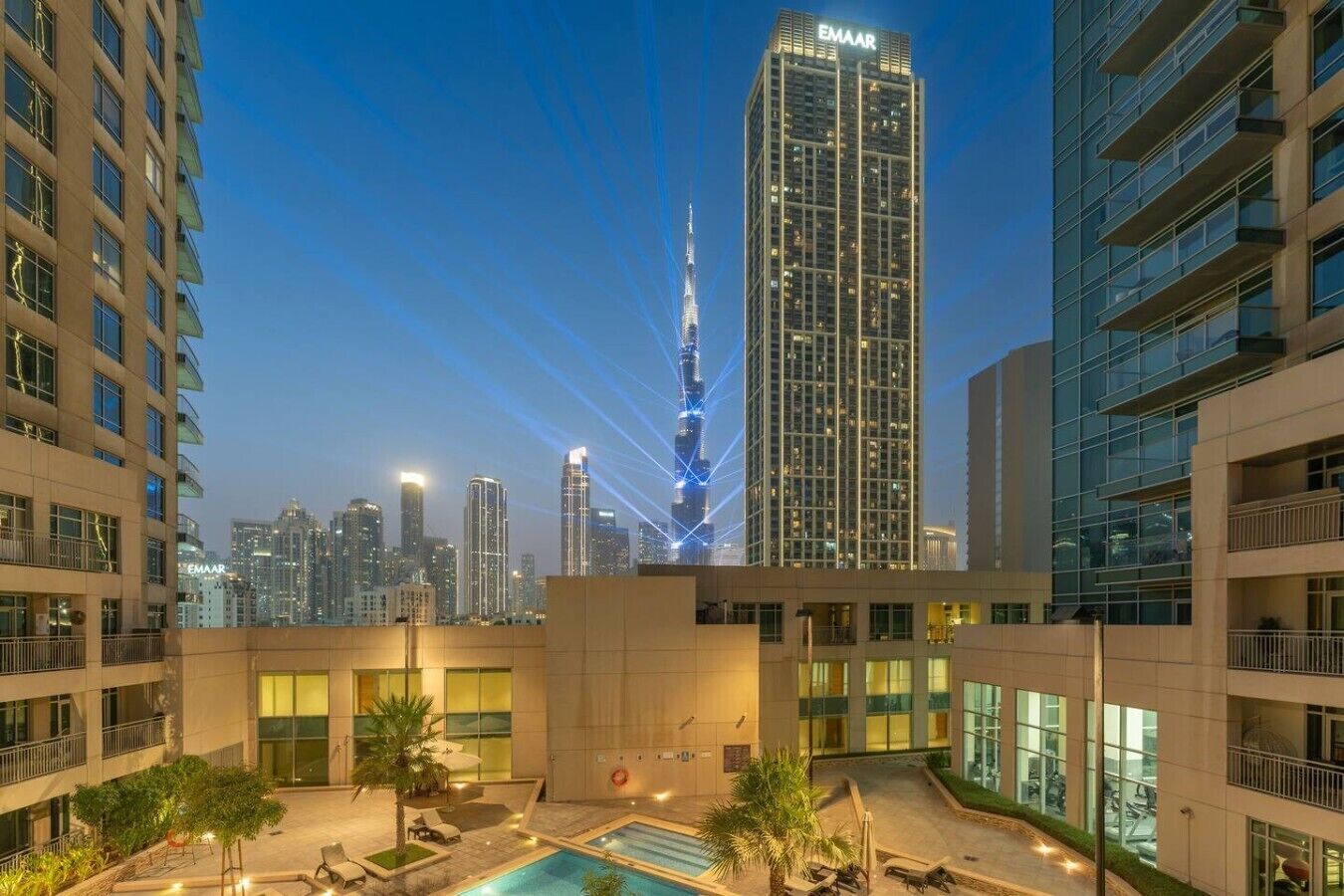 A high-rise building with a pool area in the foreground, surrounded by other buildings.