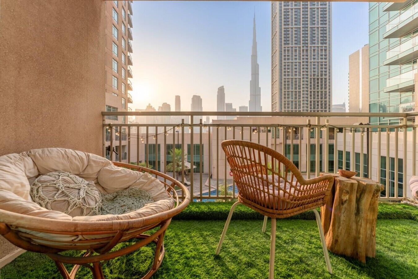 A balcony with a wicker chair and a small table, overlooking a cityscape with high-rise buildings.