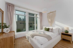 Ein modernes Schlafzimmer mit einem großen Bett, einem Nachttisch, einer Wanddekoration aus Makramee und einem Fenster mit Vorhängen.